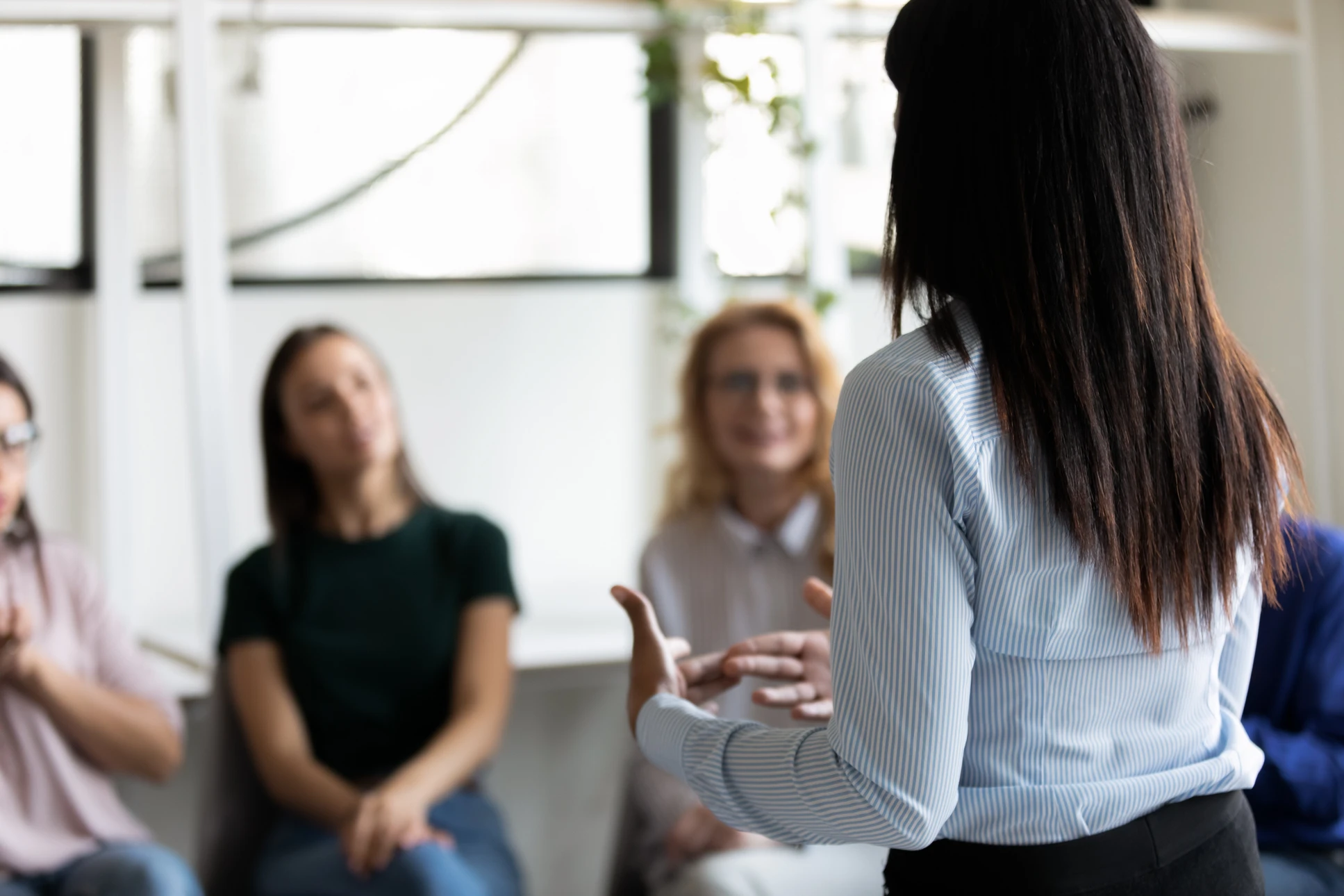 Femme en chemise rayée blanche présentant devant un groupe de professionnelles assises dans un bureau moderne
