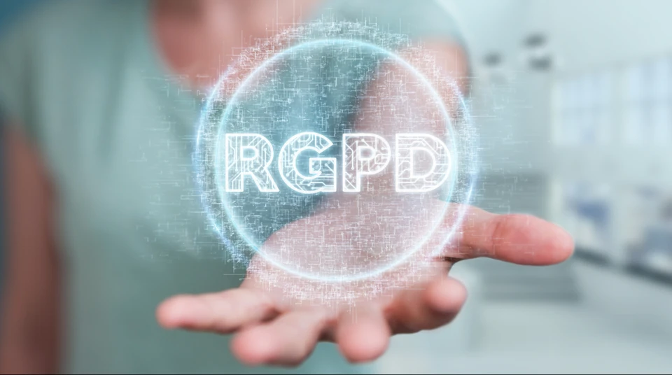 Main ouverte dans un environnement de bureau moderne présentant un hologramme numérique lumineux avec l'acronyme "RGPD" au centre d'un cercle de particules scintillantes